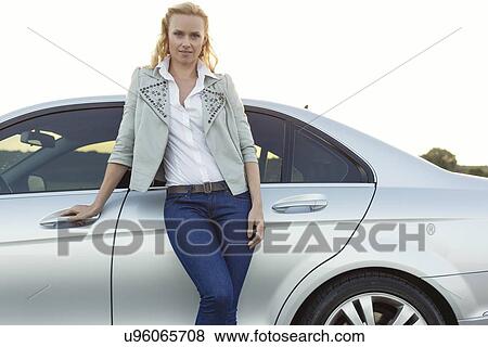 Stock Photo - Portrait of beautiful young woman standing by car at countryside. Fotosearch