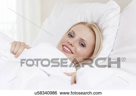 Portrait of beautiful young woman smiling while lying in bed View Large Photo Image Stock Photograph - Portrait of beautiful young woman smiling while lying in bed. Fotosearch