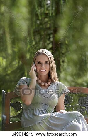 Stock Photography - Portrait of beautiful young woman using mobile phone on park bench. Fotosearch