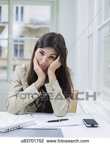 Stock Image - Portrait of bored businesswoman sitting at desk in office. Fotosearch