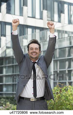 Stock Photograph - Portrait of cheerful businessman celebrating success outside office building. Fotosearch