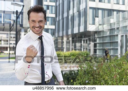 Portrait of cheerful businessman with clenched fist standing outside office building View Large Photo Image Stock Photograph - Portrait of cheerful businessman with clenched fist standing outside office building. Fotosearch