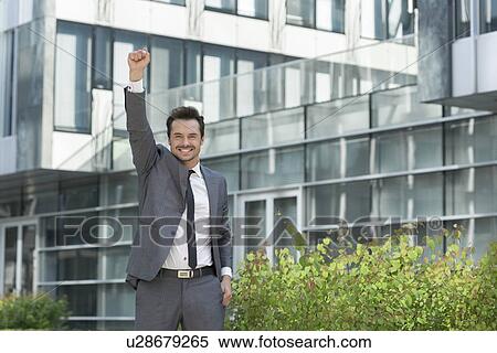 Portrait of cheerful businessman with arm raised standing outside office building View Large Photo Image Stock Photography - Portrait of cheerful businessman with arm raised standing outside office building. Fotosearch