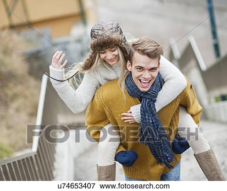 Stock Photo - Portrait of cheerful man piggybacking woman on stairway. Fotosearch
