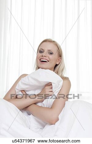 Portrait of cheerful young woman covering herself with bedsheet in bed View Large Photo Image Stock Photo - Portrait of cheerful young woman covering herself with bedsheet in bed. Fotosearch
