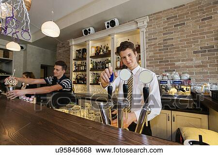 Stock Photo - Portrait of confident bartender at counter with coworkers in background. Fotosearch