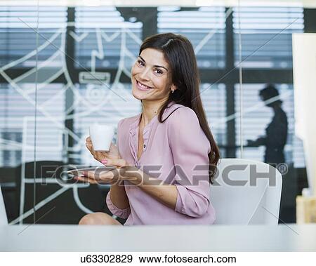 Portrait of confident businesswoman having coffee in office View Large Photo Image Stock Photo - Portrait of confident businesswoman having coffee in office. Fotosearch