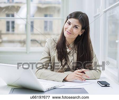 Portrait of confident businesswoman with laptop sitting at office desk View Large Photo Image Stock Photo - Portrait of confident businesswoman with laptop sitting at office desk. Fotosearch