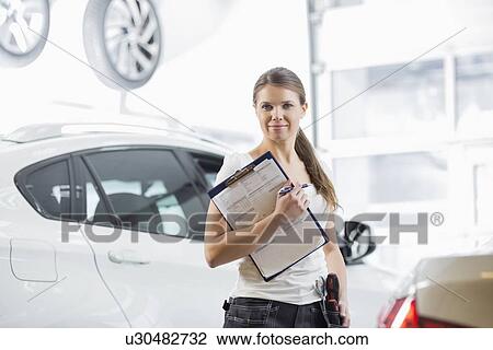 Stock Image - Portrait of confident female mechanic with clipboard in car workshop. Fotosearch