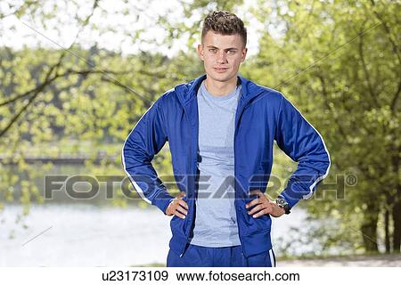 Stock Photo - Portrait of confident fit man standing with hands on hips in park. Fotosearch