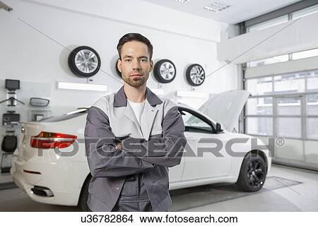 Portrait of confident male automobile mechanic standing in front of car at workshop View Large Photo Image Picture - Portrait of confident male automobile mechanic standing in front of car at workshop. Fotosearch