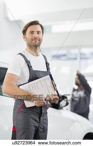 Portrait of confident male automobile mechanic with clipboard in car repair store View Large Photo Image Picture - Portrait of confident male automobile mechanic with clipboard in car repair store. Fotosearch