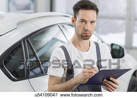 Stock Photo - Portrait of confident male maintenance engineer writing on clipboard in workshop. Fotosearch