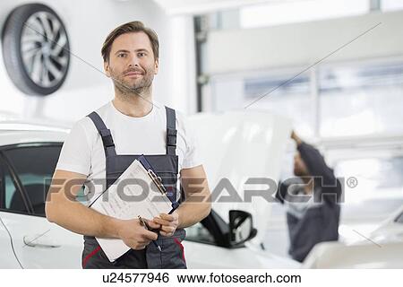 Stock Photograph - Portrait of confident male maintenance engineer with clipboard in car repair shop. Fotosearch