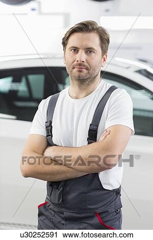 Stock Image - Portrait of confident male mechanic standing arms crossed in workshop. Fotosearch