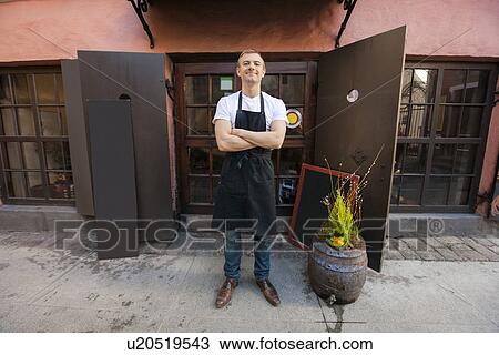 Stock Image - Portrait of confident male salesperson standing arms crossed outside coffee store. Fotosearch