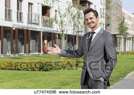 Stock Photograph - Portrait of confident real estate agent presenting office building. Fotosearch