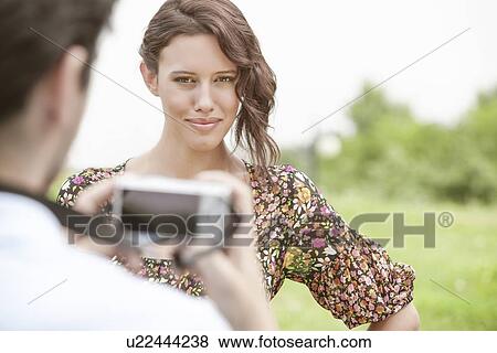 Stock Photo - Portrait of confident woman being photographed by man in park. Fotosearch