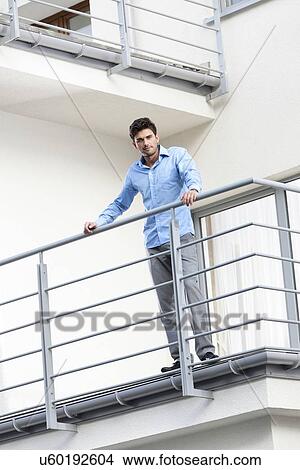 Picture - Portrait of confident young businessman standing at hotel balcony. Fotosearch