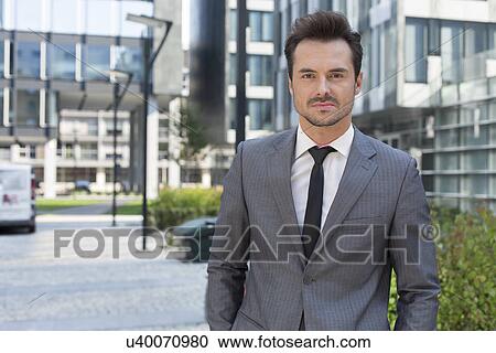 Portrait of confident young businessman standing outside office building View Large Photo Image Stock Image - Portrait of confident young businessman standing outside office building. Fotosearch