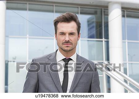 Stock Photo - Portrait of confident young businessman standing outside office building. Fotosearch