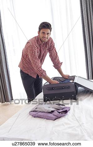 Portrait of confident young businessman unpacking suitcase on bed View Large Photo Image Stock Photo - Portrait of confident young businessman unpacking suitcase on bed. Fotosearch