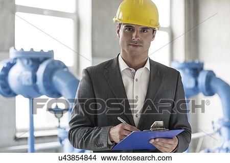 Picture - Portrait of confident young male supervisor writing on clipboard in industry. Fotosearch