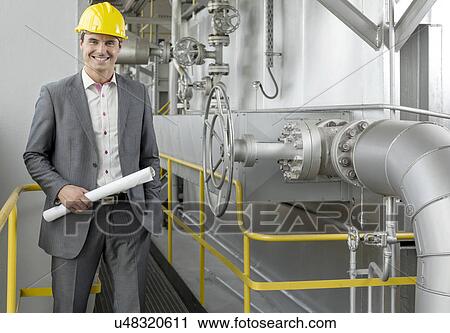 Portrait of confident young male architect holding blueprint by machinery in industry View Large Photo Image Stock Image - Portrait of confident young male architect holding blueprint by machinery in industry. Fotosearch