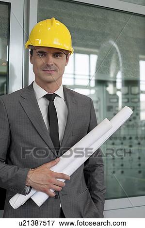 Portrait of confident young male architect holding blueprints in industry View Large Photo Image Stock Photo - Portrait of confident young male architect holding blueprints in industry. Fotosearch