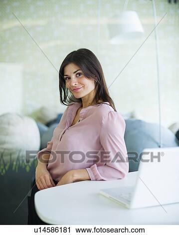 Stock Image - Portrait of confident young businesswoman leaning at office table. Fotosearch