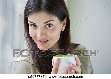 Stock Image - Portrait of confident young businesswoman with coffee cup in office. Fotosearch