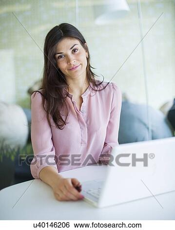 Portrait of confident young businesswoman using laptop at office table View Large Photo Image Stock Photograph - Portrait of confident young businesswoman using laptop at office table. Fotosearch