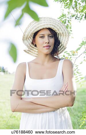 Portrait of confident young woman in sundress and hat standing arms crossed in park View Large Photo Image Stock Image - Portrait of confident young woman in sundress and hat standing arms crossed in park. Fotosearch