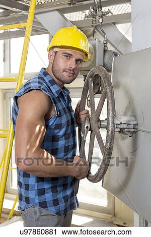 Stock Image - Portrait of confident young worker fixing industrial valve. Fotosearch