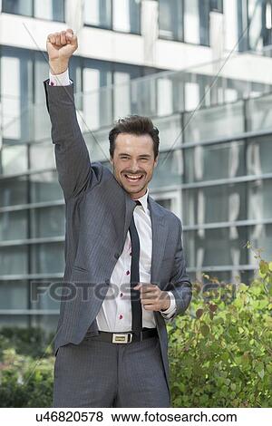 Stock Photo - Portrait of excited businessman with arm raised celebrating success outside office building. Fotosearch