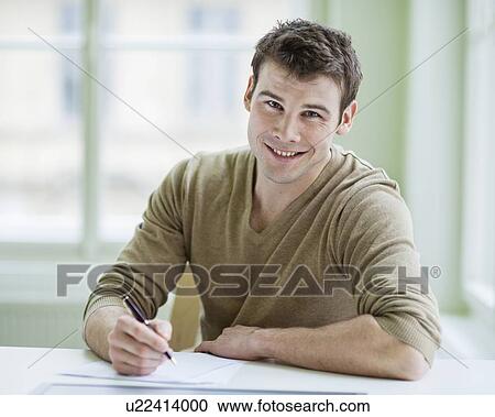 Stock Image - Portrait of handsome businessman writing on document at desk in office. Fotosearch