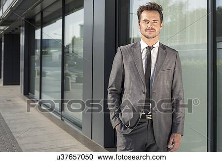 Portrait of handsome young businessman standing outside office building View Large Photo Image Stock Image - Portrait of handsome young businessman standing outside office building. Fotosearch