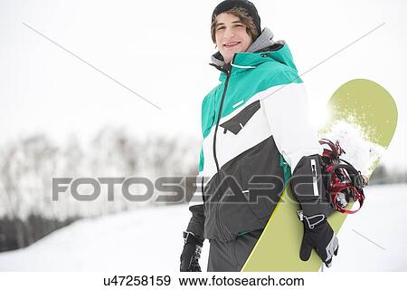 Stock Photo - Portrait of handsome young man with snowboard in snow. Fotosearch