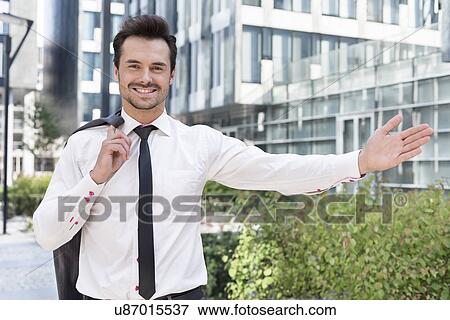 Stock Photo - Portrait of happy businessman gesturing while standing outside office building. Fotosearch