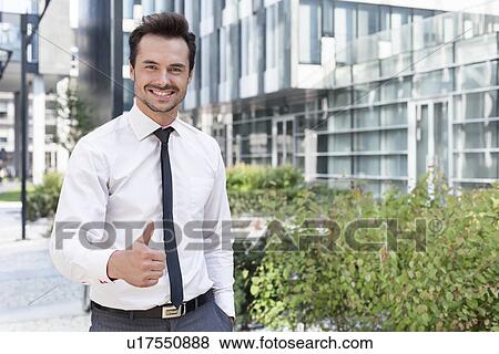 Portrait of happy businessman showing thumbs up outside office building View Large Photo Image Stock Photo - Portrait of happy businessman showing thumbs up outside office building. Fotosearch