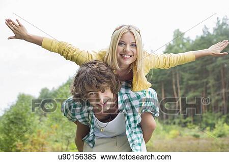Portrait of happy woman enjoying piggyback ride on man in forest View Large Photo Image Stock Photography - Portrait of happy woman enjoying piggyback ride on man in forest. Fotosearch