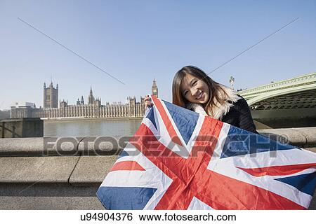 Stock Photograph - Portrait of happy woman holding British flag against Big Ben at London, England, UK. Fotosearch