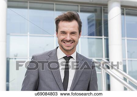 Portrait of happy young businessman standing outside office building View Large Photo Image Stock Image - Portrait of happy young businessman standing outside office building. Fotosearch