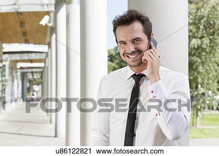 Portrait of happy young businessman using mobile phone outside office View Large Photo Image Stock Image - Portrait of happy young businessman using mobile phone outside office. Fotosearch
