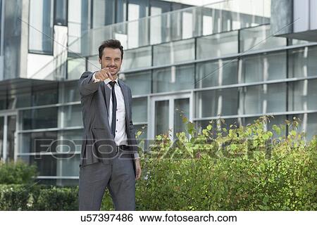 Stock Photograph - Portrait of happy young businessman pointing at you outside office building. Fotosearch