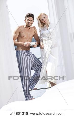Stock Photo - Portrait of happy young couple in sleepwear having coffee at hotel balcony. Fotosearch