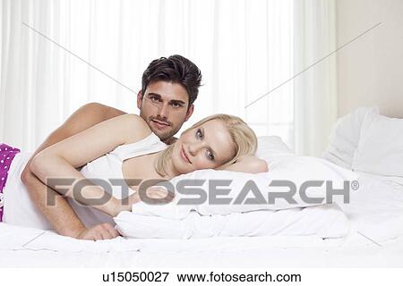 Portrait of happy young couple lying in bed View Large Photo Image Stock Photo - Portrait of happy young couple lying in bed. Fotosearch
