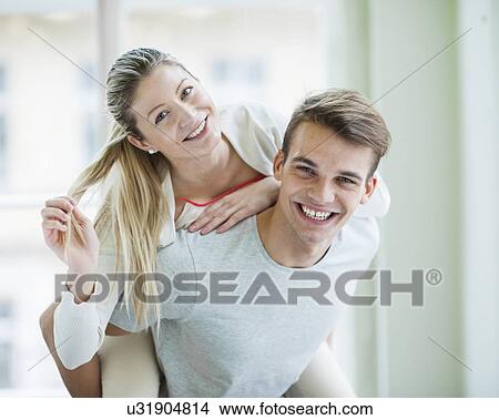 Portrait of happy young man giving piggyback ride to woman at home View Large Photo Image Picture - Portrait of happy young man giving piggyback ride to woman at home. Fotosearch