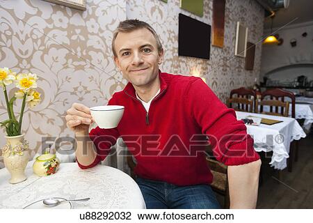 Stock Image - Portrait of happy young man holding coffee cup at cafe. Fotosearch