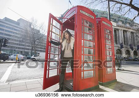 Stock Photograph - Portrait of happy young woman opening door of telephone booth at London, England, UK. Fotosearch